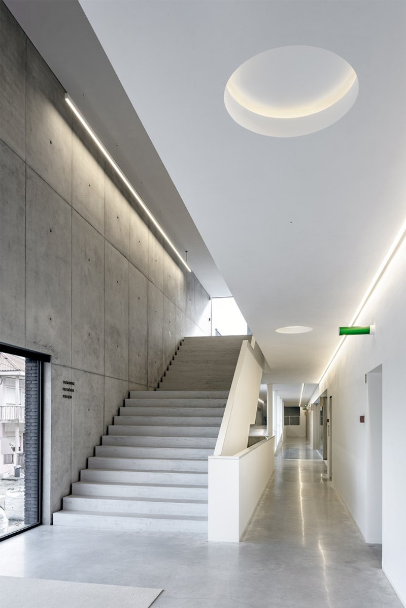 Concrete staircase leading to an upper level beneath a circular skylight with recessed illumination