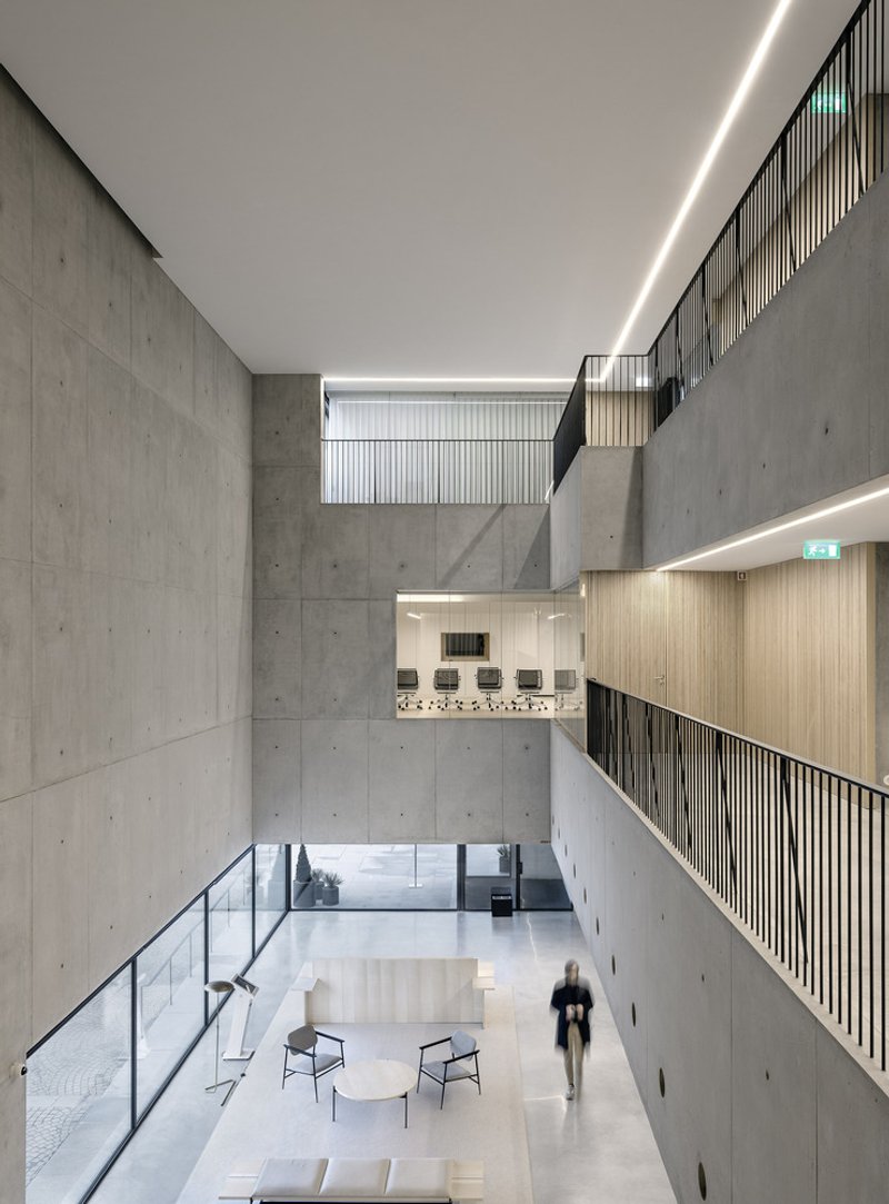Multi-story atrium with board-formed concrete walls, timber-lined balconies and a person walking below