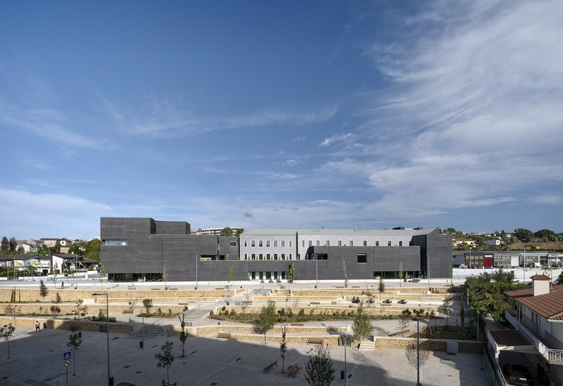 Wide view of the gray concrete volumes flanking a terraced public plaza with young trees