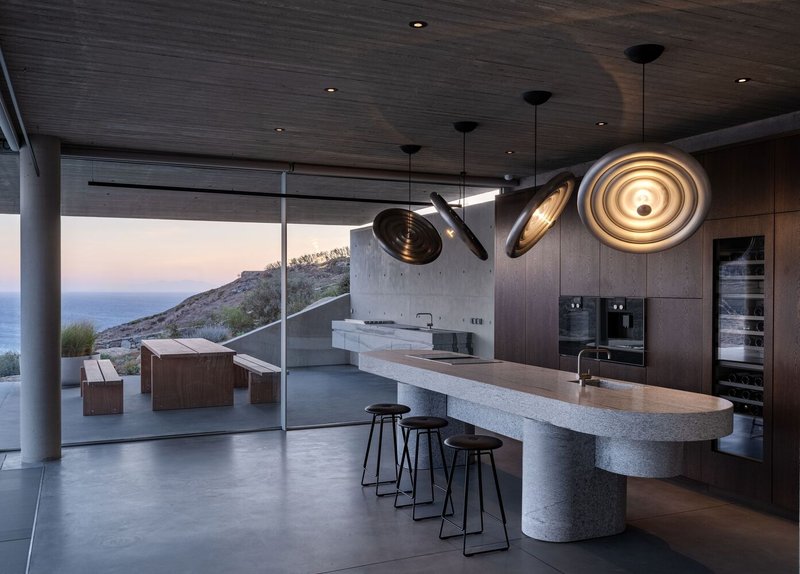 Kitchen island with curved stone counter and pendant lights opening to terrace at twilight