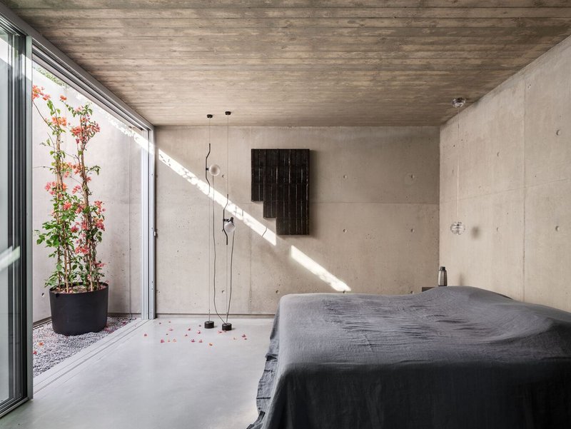 Bedroom with concrete walls and a small courtyard garden visible through glazed sliding door