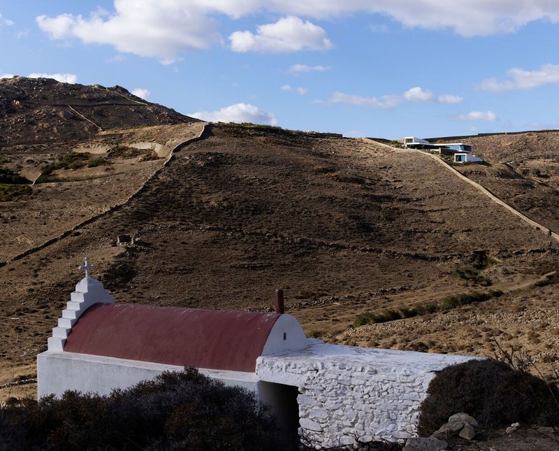 White chapel with burgundy barrel vault and stepped bell tower in a rugged hillside setting