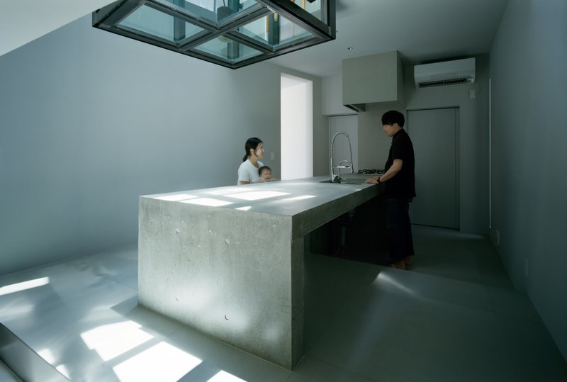 Concrete kitchen island with two people under glass ceiling skylight in afternoon light