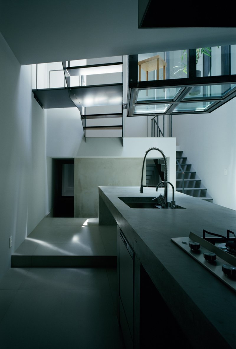 Double-height kitchen space with suspended steel staircase and glass floor bridge illuminated by skylights