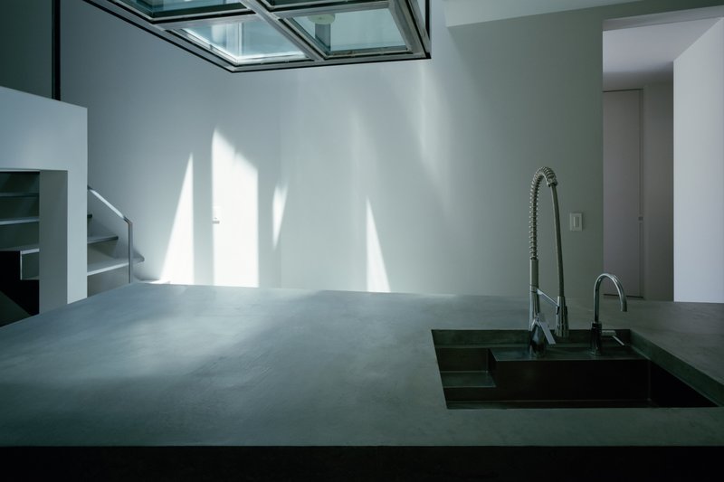 Concrete countertop with recessed sink under grid skylight casting sharp shadows on white walls