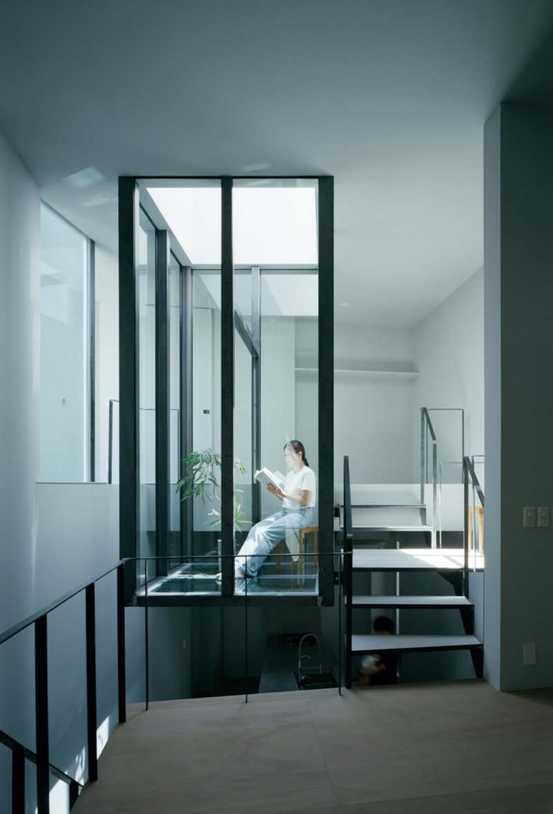 Glass-enclosed reading nook with steel staircase and person seated with greenery inside
