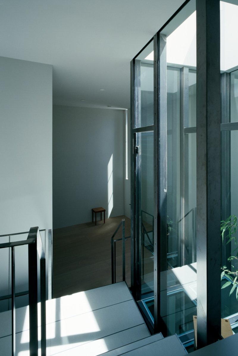 Stairwell with black steel handrail and glass partition framing a white-walled landing in afternoon sunlight