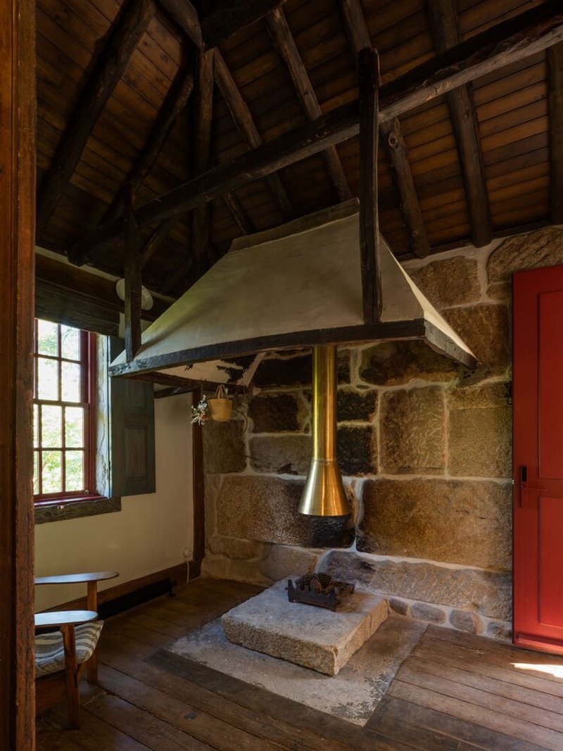 Interior hearth with stone base and white plaster hood beneath exposed timber roof beams and boarding