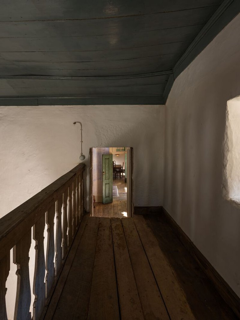 Timber balustrade along a narrow hallway with whitewashed walls and dark stained ceiling boards