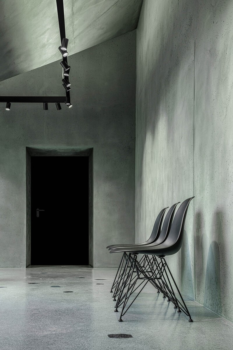 Interior corridor with board-formed concrete walls, stacked wire-frame chairs and black track lighting overhead