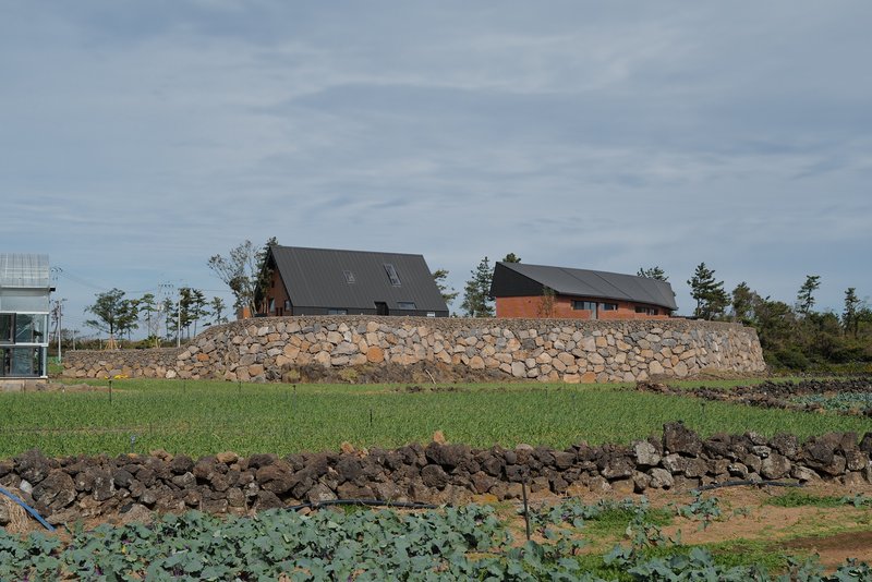 Two dark-roofed volumes atop a stone retaining wall rising from terraced agricultural fields