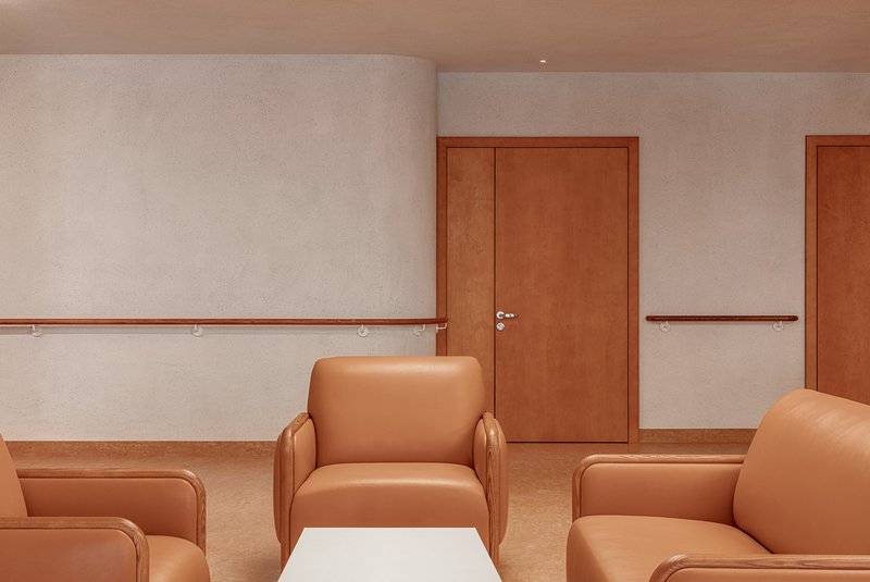 Corridor with tan upholstered armchairs, timber handrails, and wood doors along a white wall