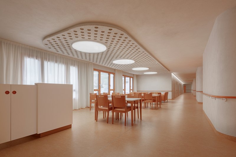 Dining hall with perforated curved ceiling panels and round skylights over timber furniture and rubber flooring