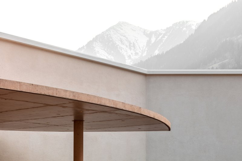 Cantilevered canopy with timber soffit and exposed edge against snow-dusted alpine peaks