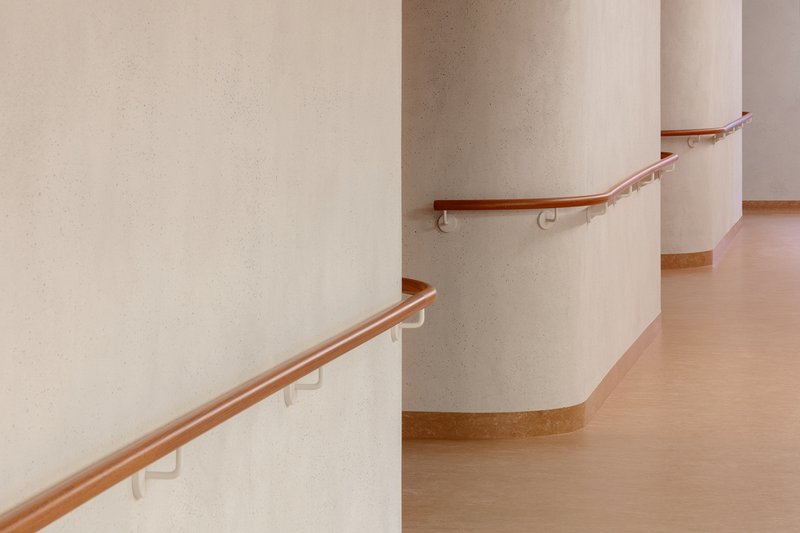 Curved corridor with timber handrails mounted on white walls and continuous rubber base trim