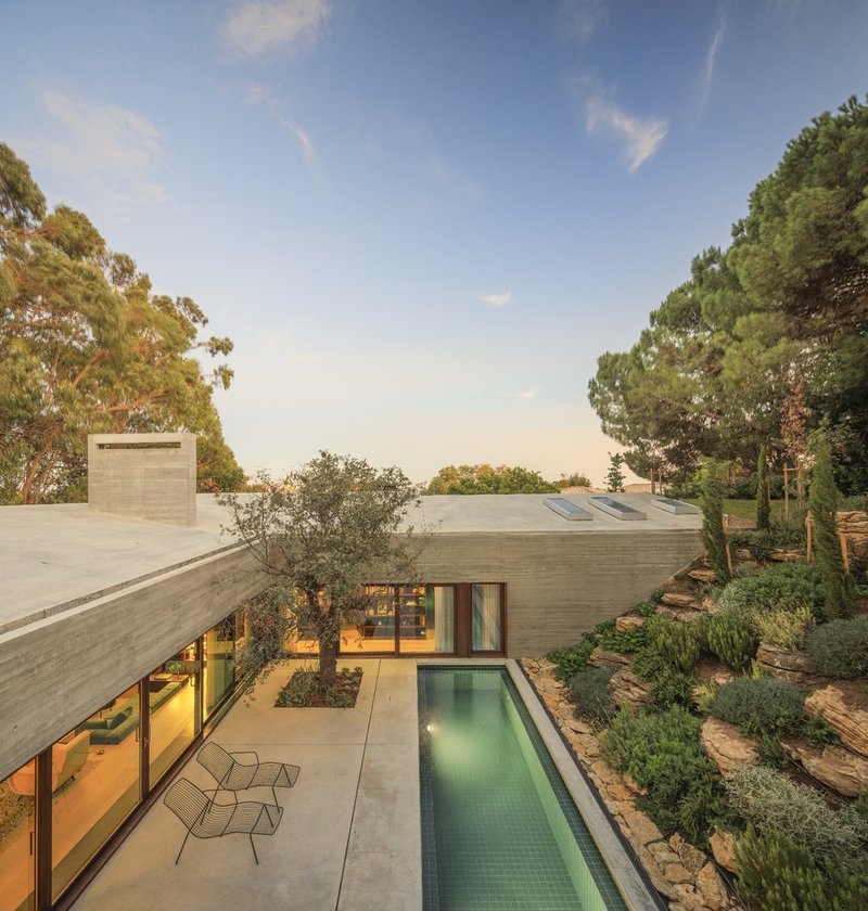 Elevated view of the concrete cantilevered roof over the courtyard pool and terraced hillside planting at dusk