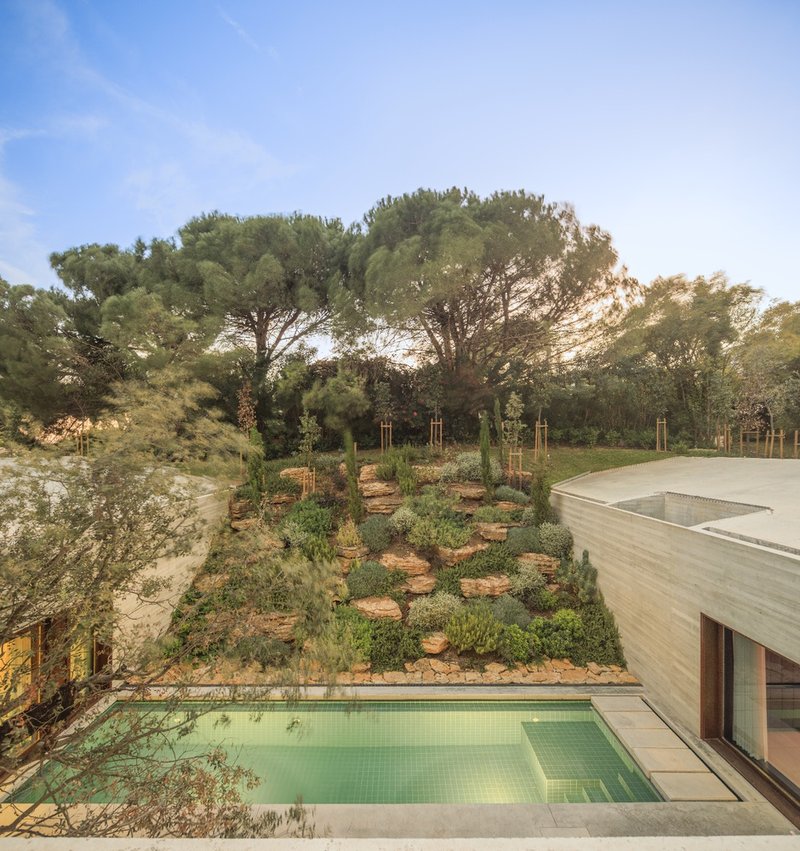 View across the planted hillside terraces and lap pool toward the concrete roof at golden hour