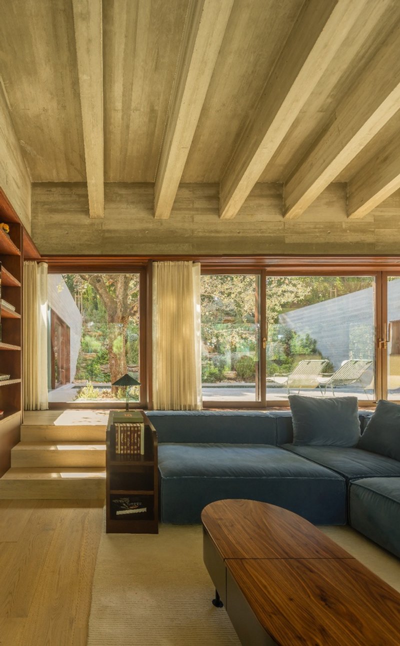 Living room with exposed timber ceiling joists and full-height glazing opening to a garden terrace with lounge chairs