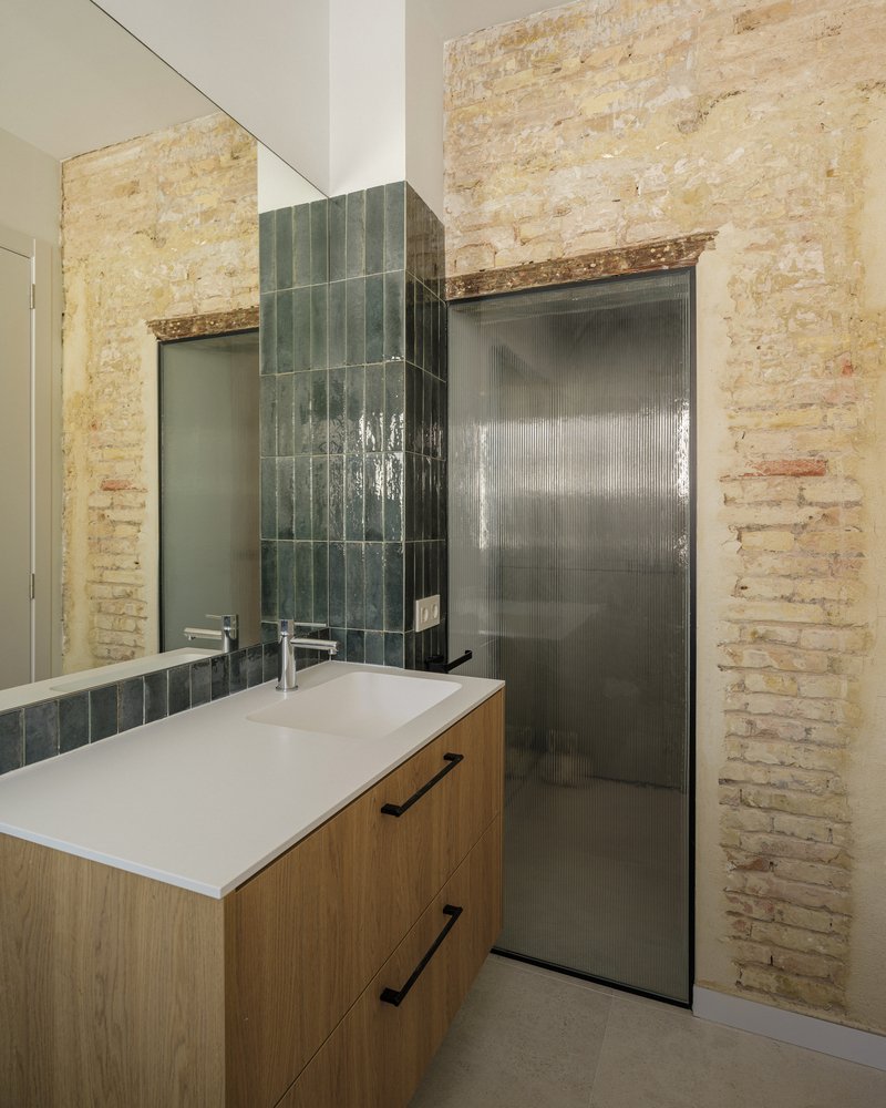 Bathroom vanity with green zellige tile backsplash against exposed brick walls
