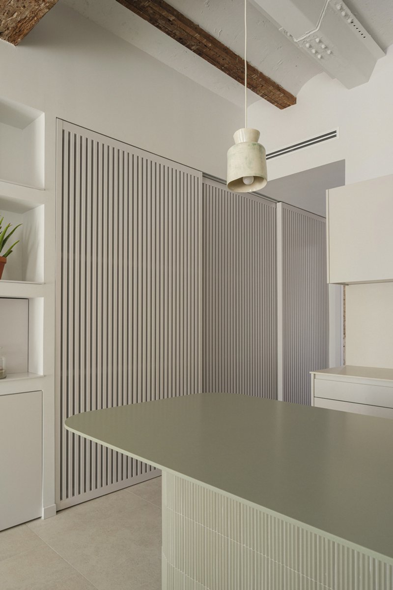 Fluted partition wall with integrated counter beneath exposed timber beams and white vaulted ceiling