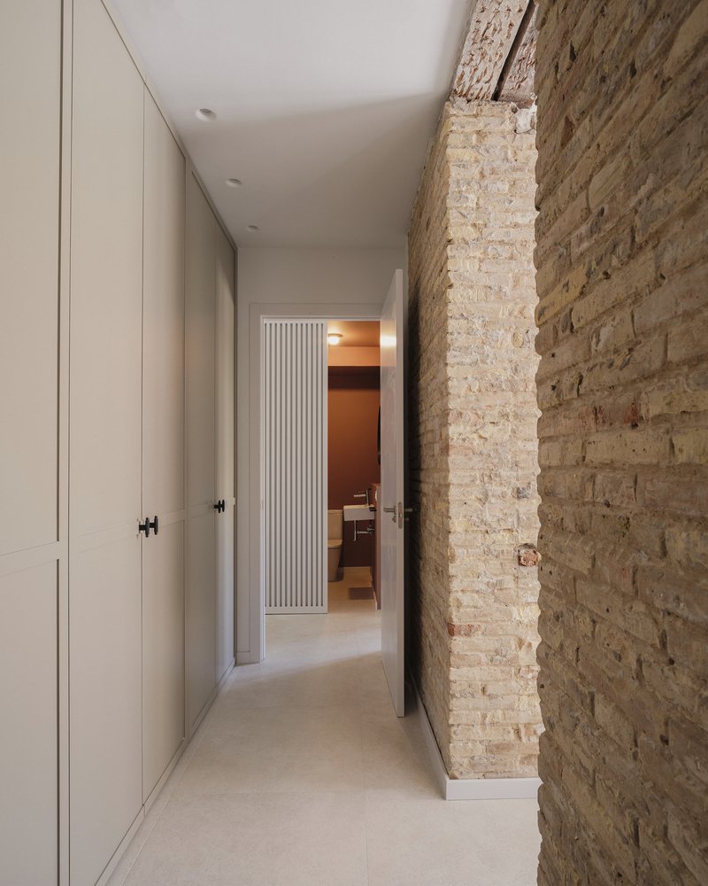 Narrow hallway with white cabinetry and exposed weathered brick wall leading toward fluted doorway