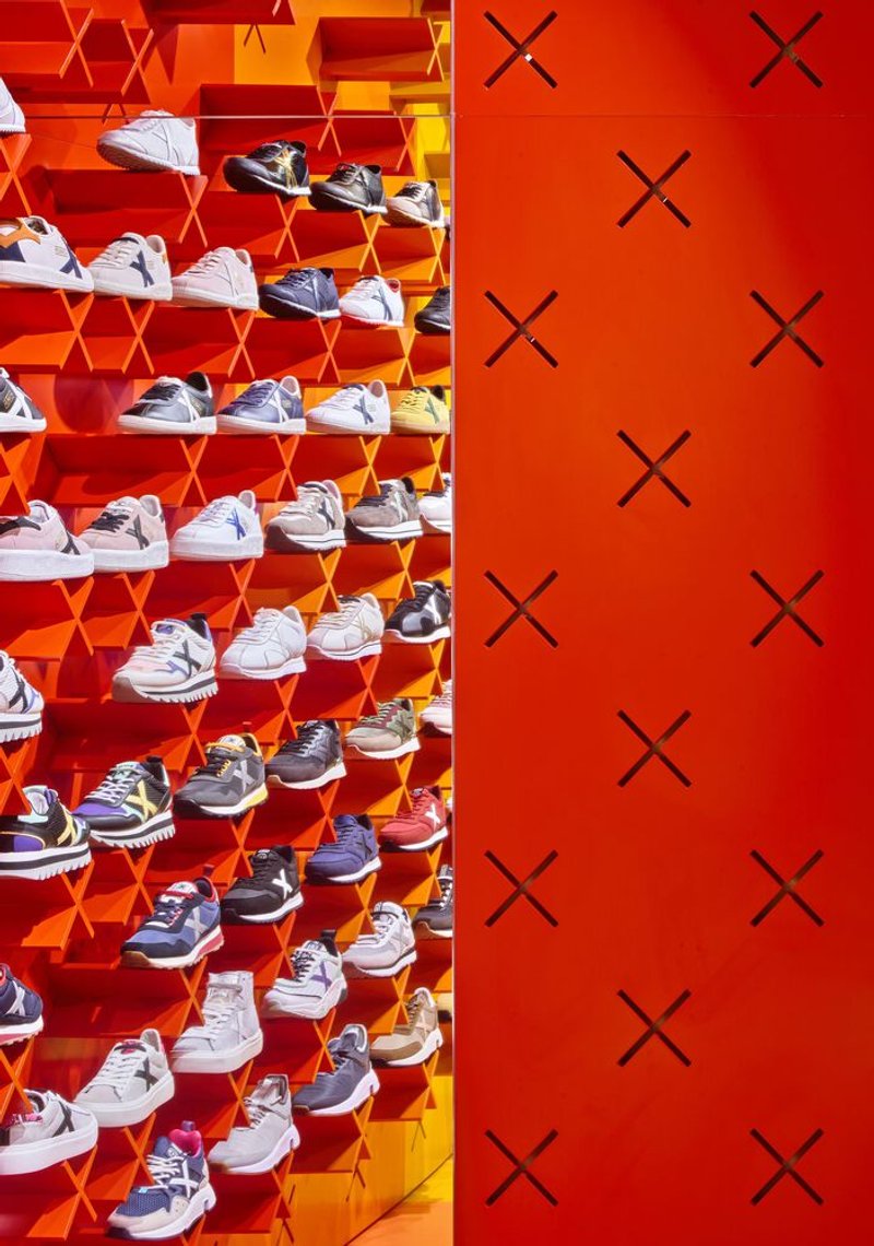Detail of cantilevered box shelves holding sneakers alongside a red wall panel with cross motifs