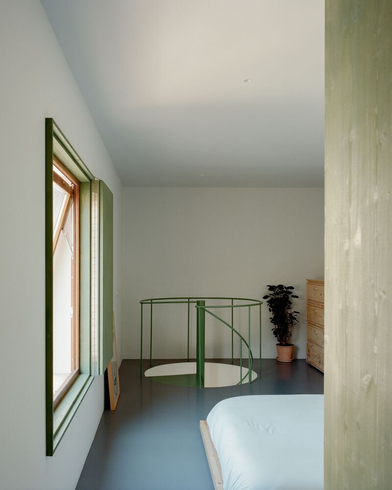 Upper-level bedroom with green window reveal and steel balustrade enclosing the spiral stair opening