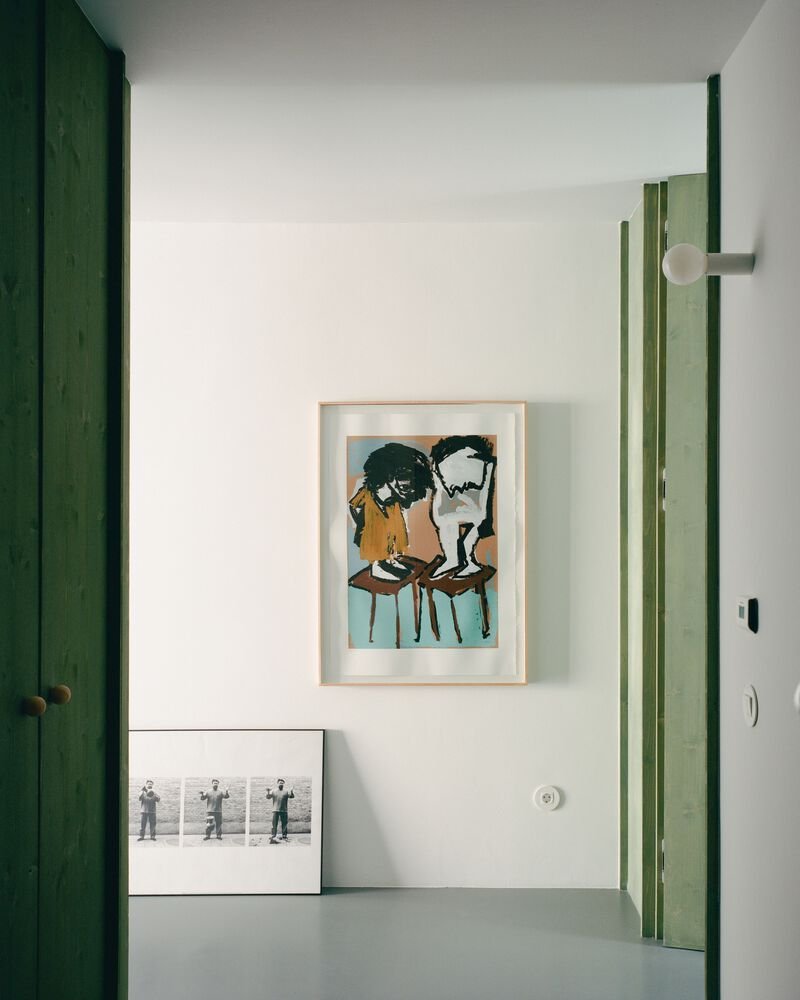 Interior corner with green timber door frames and framed artworks leaning against white walls