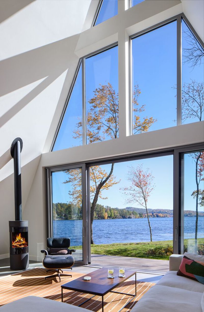 Double-height living room with floor-to-ceiling windows overlooking the lake and a wood-burning stove