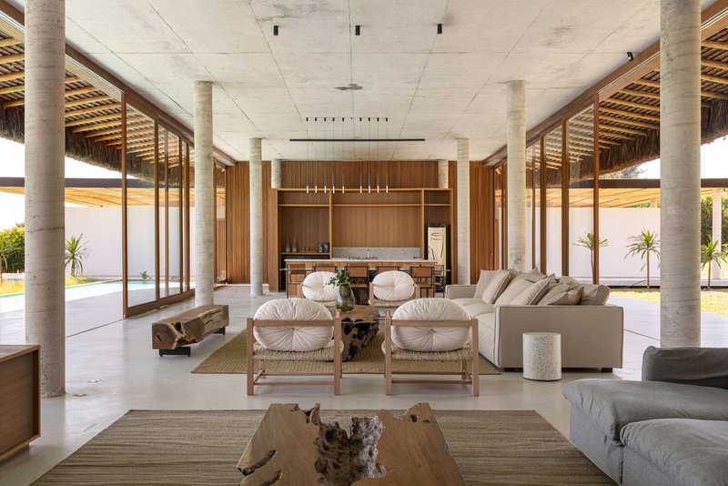 Open plan living space with exposed concrete ceiling, timber screens, and glazed walls overlooking the lawn