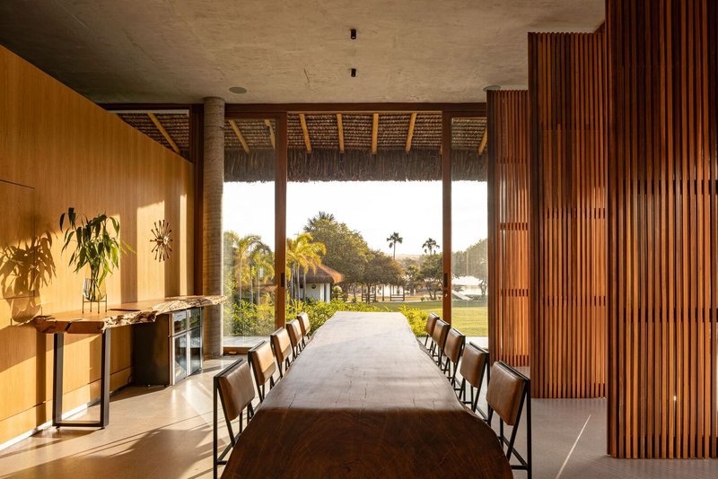 Long dining table flanked by vertical timber screen and timber-framed glazing opening to landscape