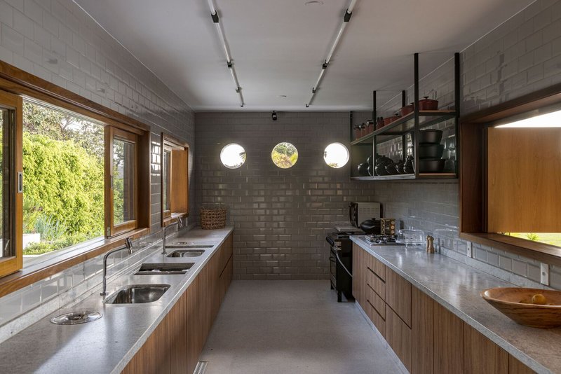 Galley kitchen with concrete block walls, timber cabinetry and three circular windows
