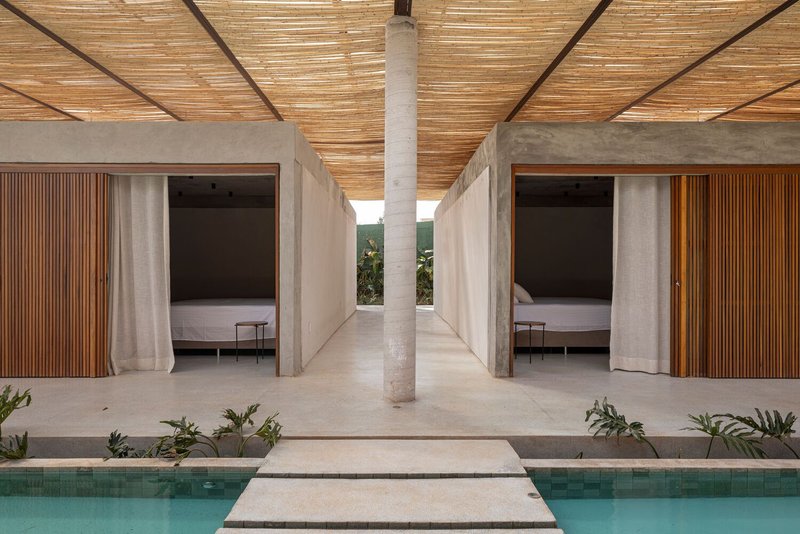 Poolside pavilion with concrete columns, slatted timber ceiling, and symmetrical bedroom openings flanking a central corridor