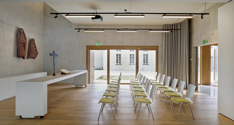 Chapel interior with white altar, rows of seating facing glazed doors opening to a paved courtyard