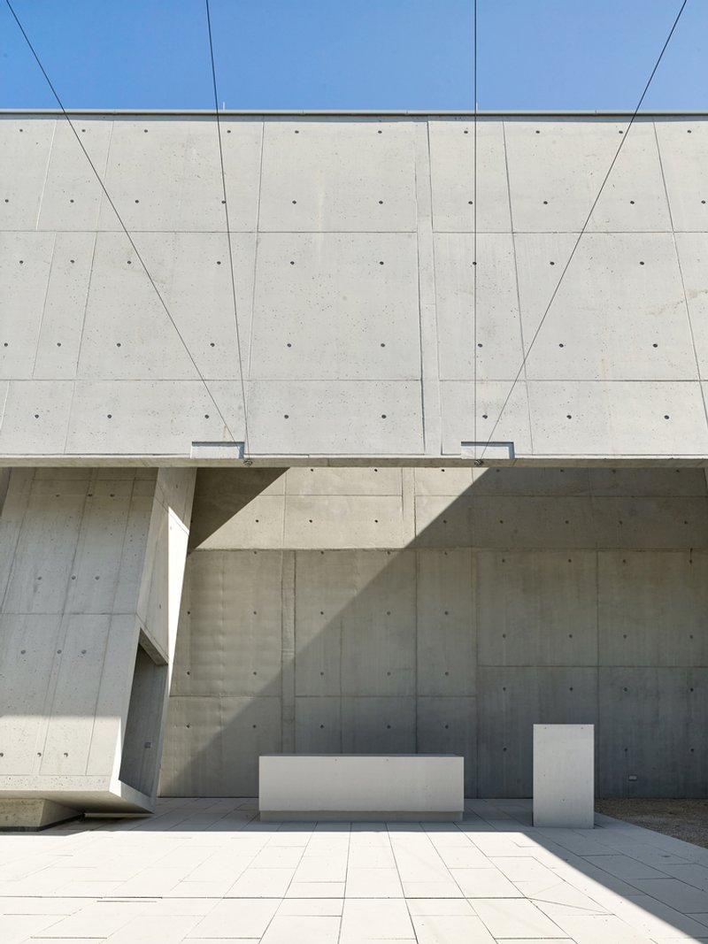 Exterior courtyard corner showing white altar and lectern against board-formed concrete walls under clear sky