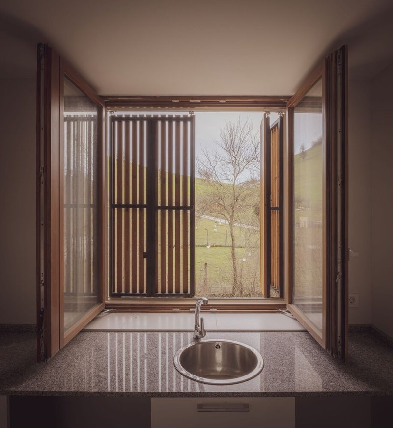 Interior window bay with timber frame and vertical screen opening to hillside with bare tree