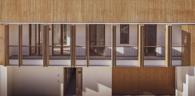Interior corridor with vertical timber shutters across glass balconies under slatted timber soffit at twilight