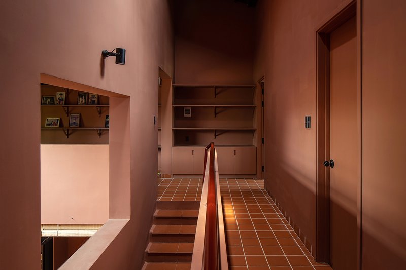Upper hallway with terracotta tile floor, timber handrail, and built-in storage under soft evening light