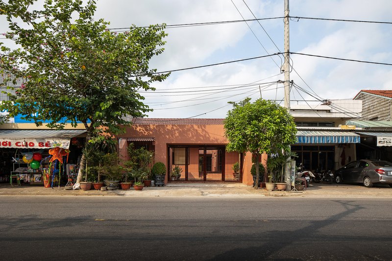 Street view of the terracotta-colored brick facade with timber doors flanked by potted plants and overhead power lines