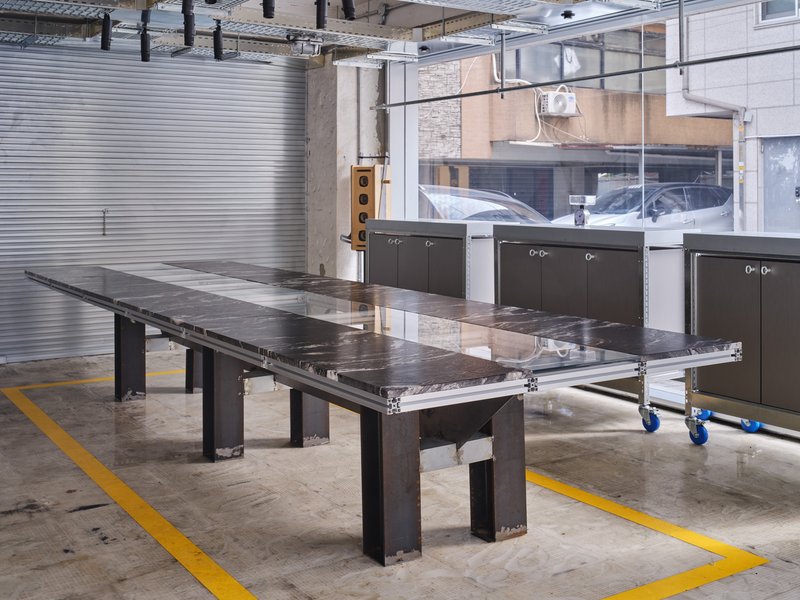 Industrial workshop space with steel work tables and dark metal cabinets beneath corrugated metal cladding
