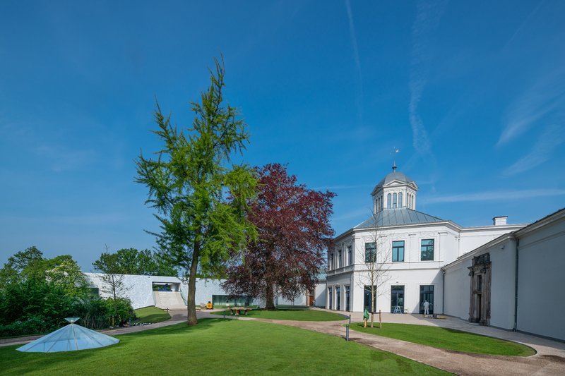 Lawn connecting the white volumes to a historic domed building under clear blue sky