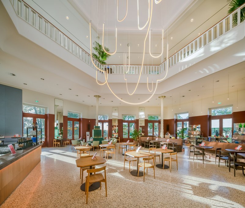 Double-height dining space with terrazzo floor and suspended curvilinear light fixture above wooden tables