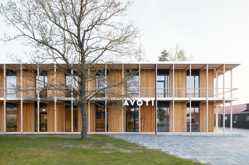 Two-storey timber-clad facade with vertical slat screens and white columns behind a bare tree in the plaza