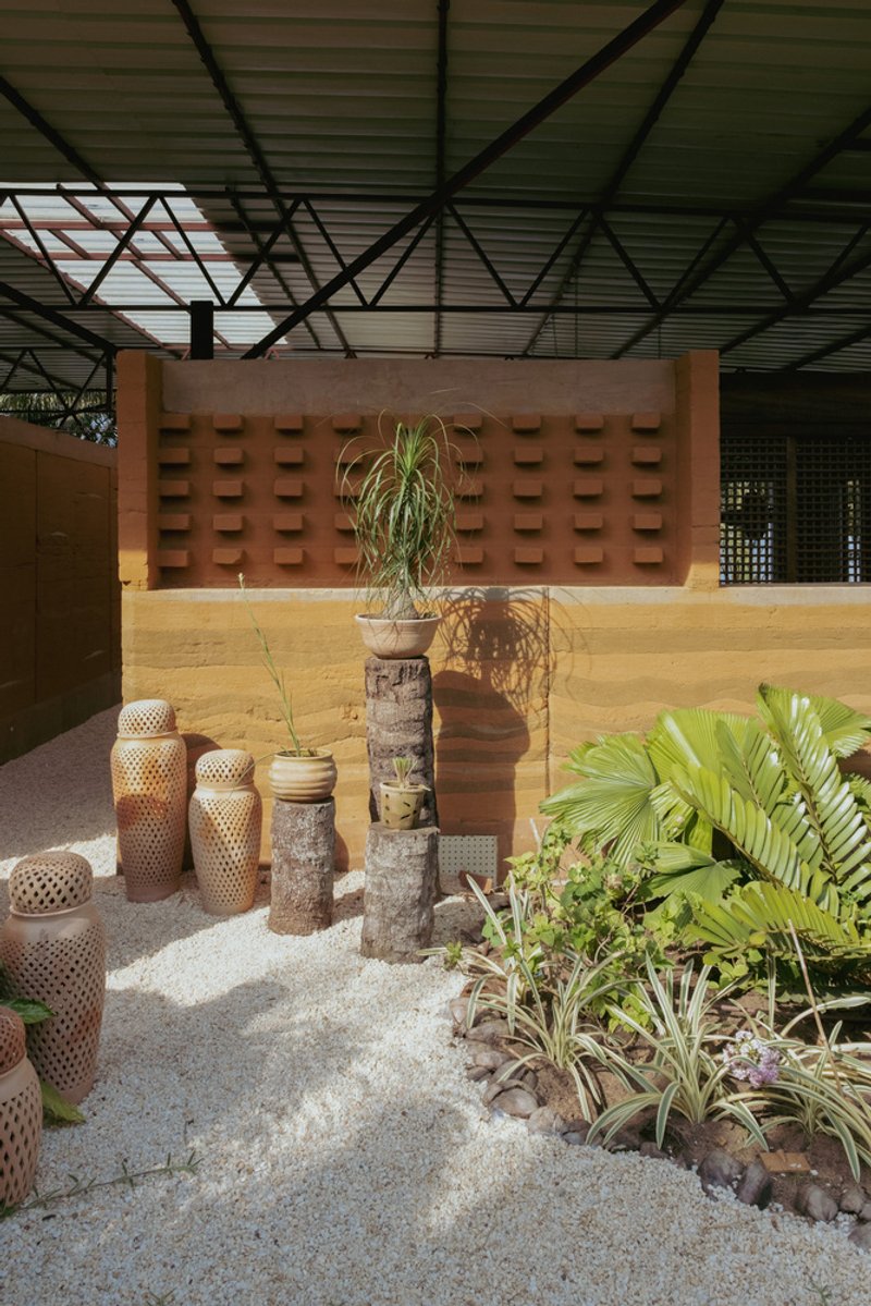 Courtyard with perforated rammed earth wall behind sculptural planters and tropical foliage in daylight