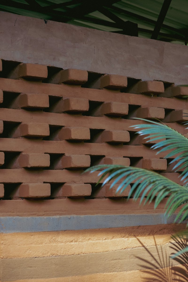 Perforated terracotta brick screen wall with palm fronds casting shadows below painted timber beams
