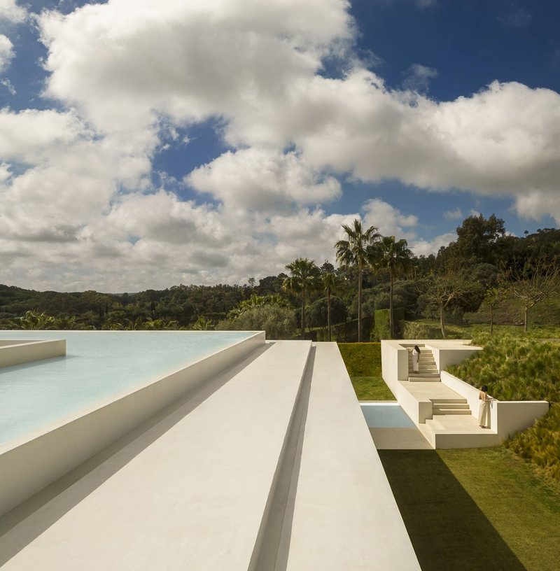 White terraced volumes stepping down the lawn toward palm trees under a cloudy sky