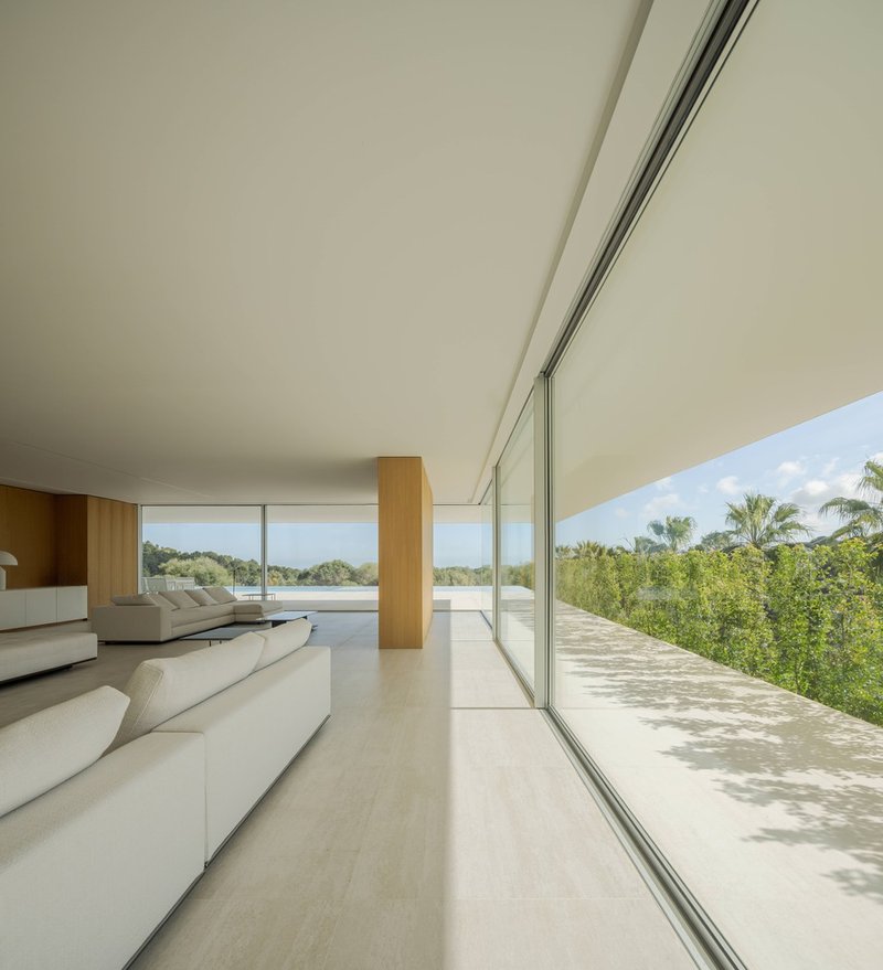 Living room with full-height glazing opening to a sun-dappled terrace and lush vegetation beyond