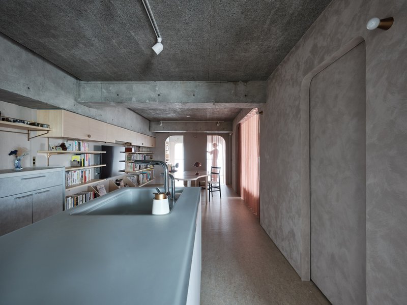 Long galley kitchen with concrete ceiling beam and rose curtains framing distant bedroom