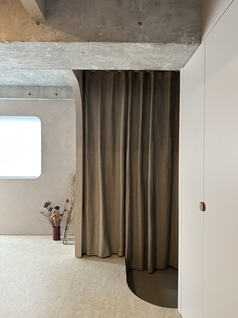 Curved brown fabric curtain suspended from exposed concrete ceiling near dried flowers in glass vases
