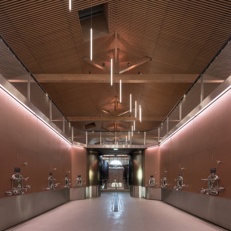 Gallery hall with timber slat ceiling, pendant linear fixtures, and bronze metal walls displaying sculptural exhibits